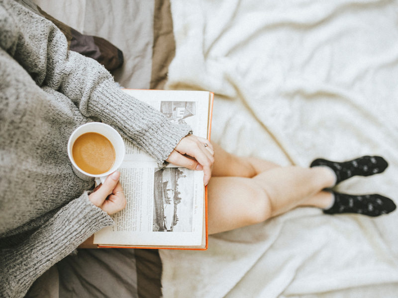 Woman reading in bed with mug of coffee