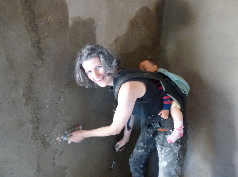Mom Claire Kenny works on mudhouse with baby on her back